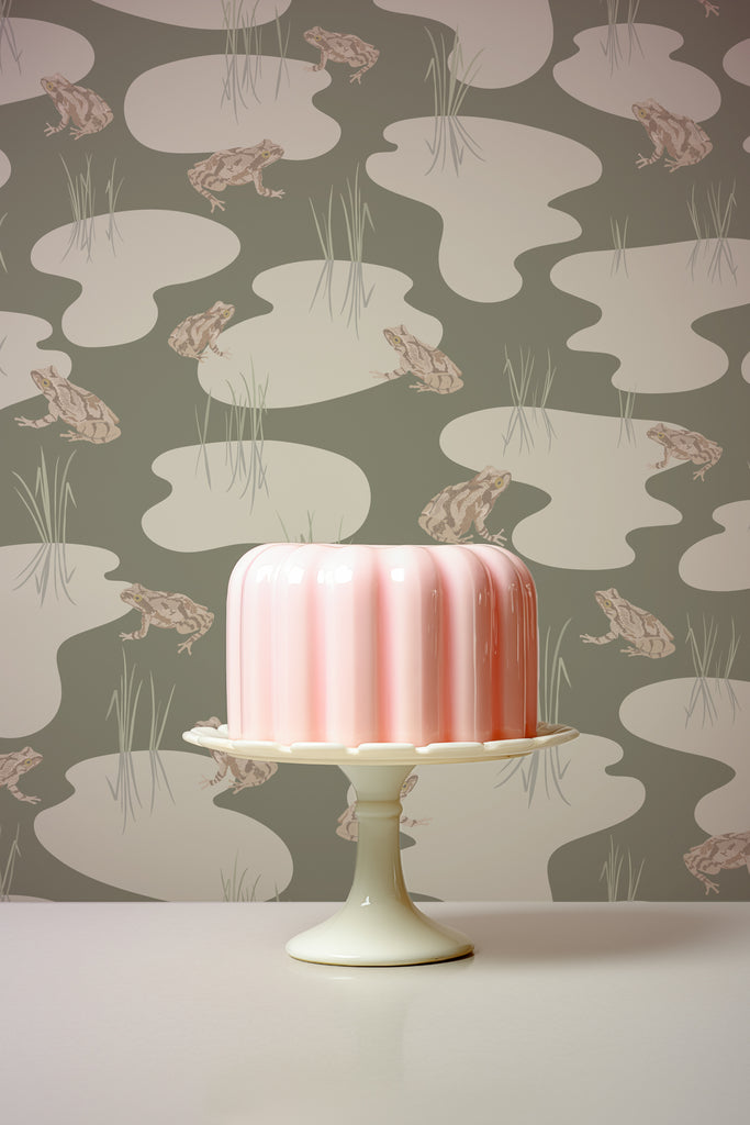 Elegant pink cake close-up against the backdrop of Kate Golding's Spring Peeper Khaki wallpaper, highlighting the wallpaper's subtle elegance and the cake's intricate design.