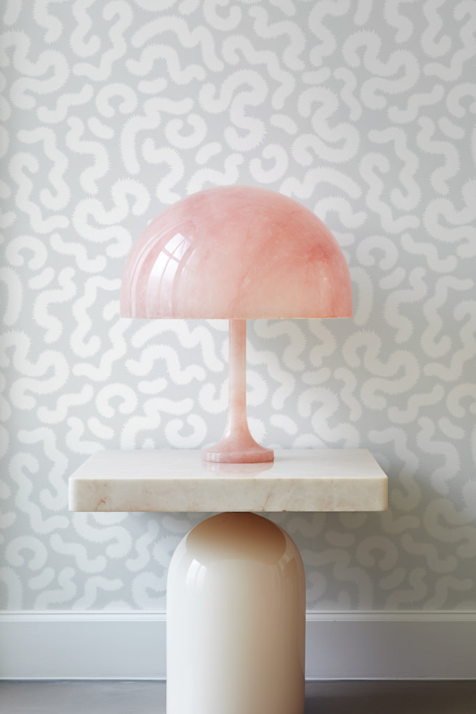 Elegant tulip lamp on an off-white marble table against the backdrop of Kate Golding's Spring Pop Silvery Grey wallpaper, showcasing refined interior aesthetics.