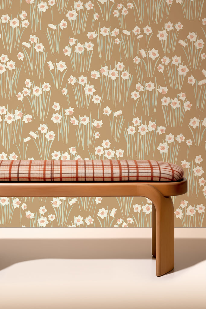 Modern interior with Daffodil Saddle Brown wallpaper showcasing elegant white daffodils with subtle peach centers on a warm saddle brown background, complementing a bench with a plaid cushion.